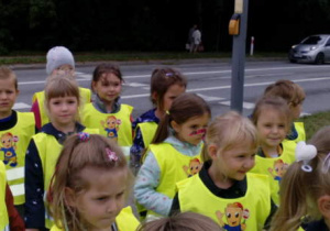 Grupa dzieci w kamizelkach odblaskowych przechodzi przez ulicę.